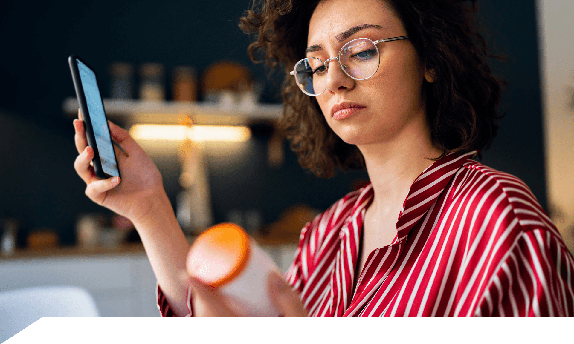 Woman holding phone looking at a bottle of pills