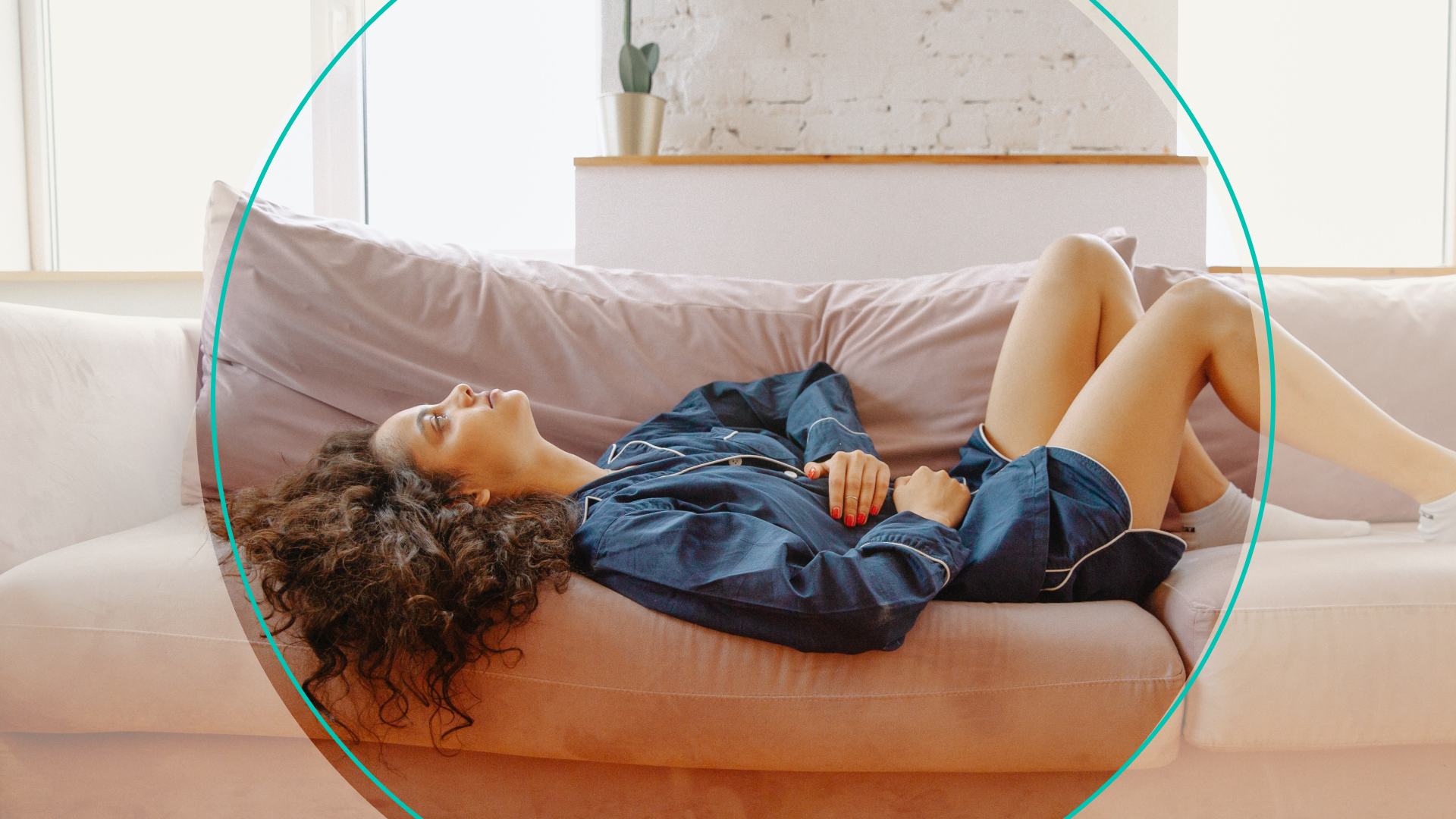 Woman laying on couch in pajamas holding stomach