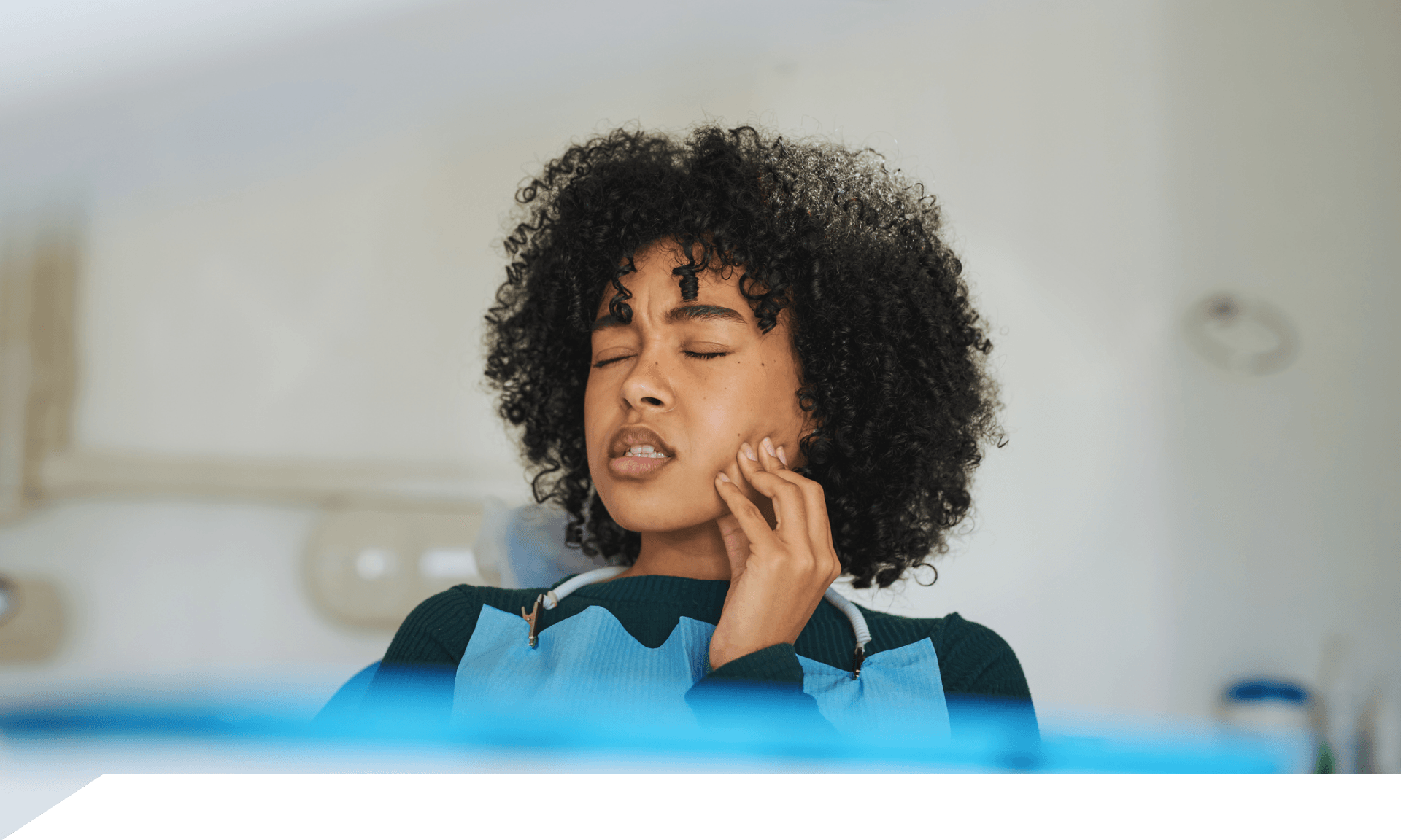 A woman in a dental chair rubbing her jaw looking uncomfortable